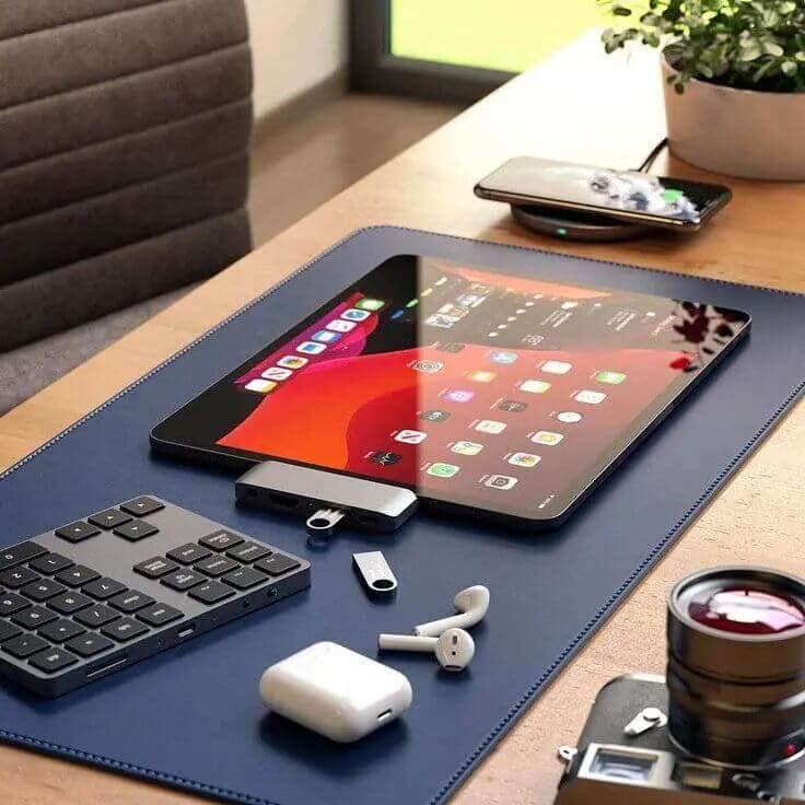 Modern workspace featuring a tablet, keyboard, AirPods, and camera on a stylish desk mat for tech enthusiasts.